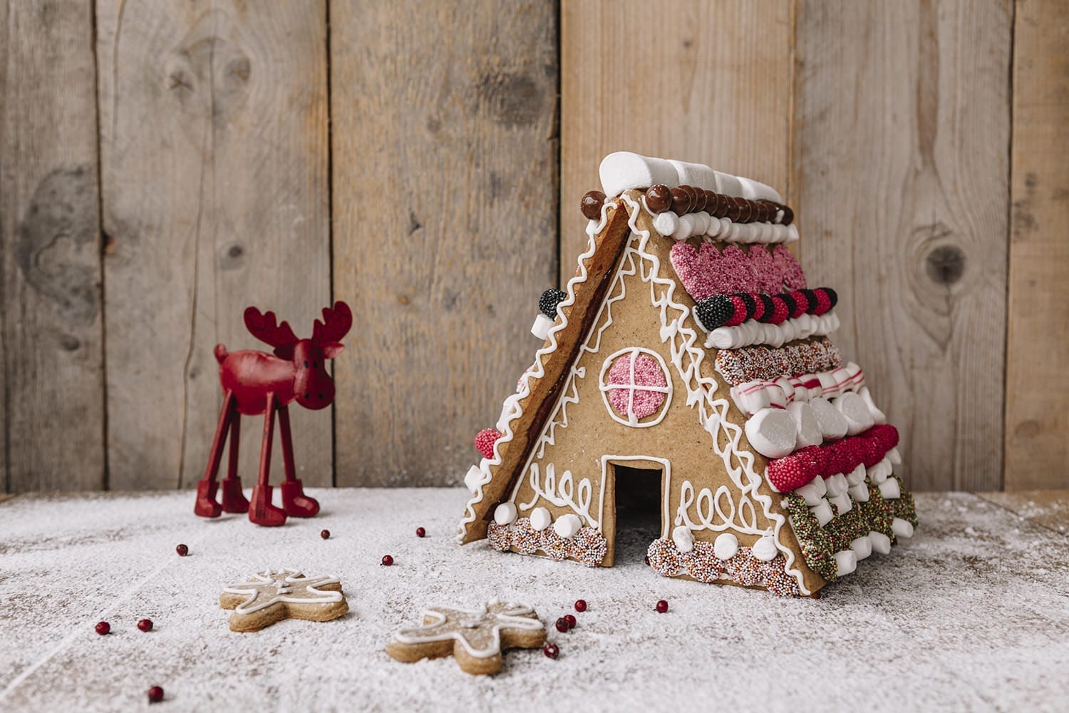 homemade scandinavian gingerbread house with lots of sweets on a snowy surface and with gingerbread men