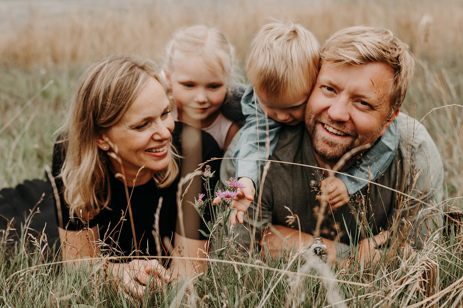 Een gezinsfotoshoot buiten in het hoge gras met een bloem in de handen.