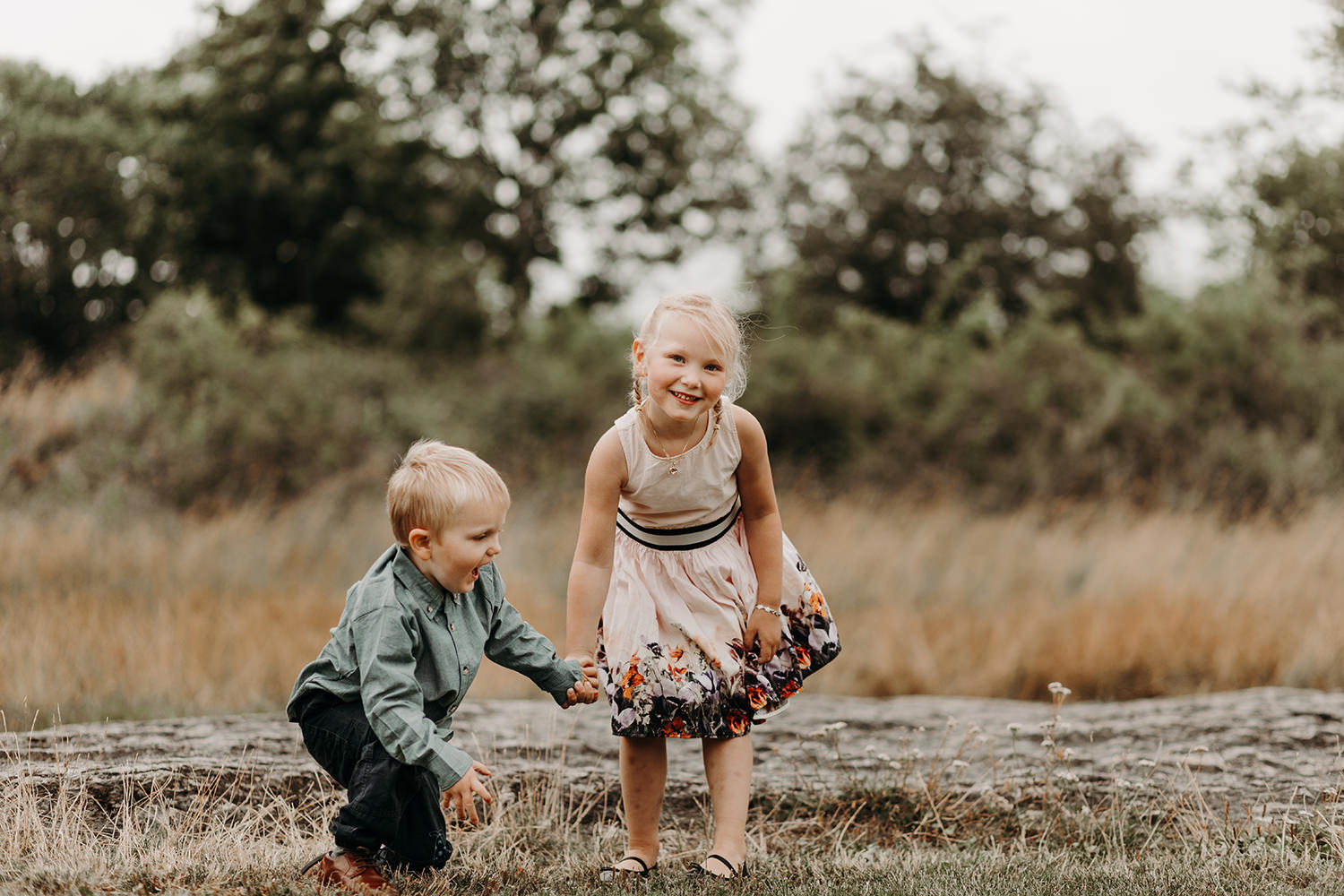 Een jongen en een meisje spelen in een veld tijdens een gezinsfotoshoot buiten.