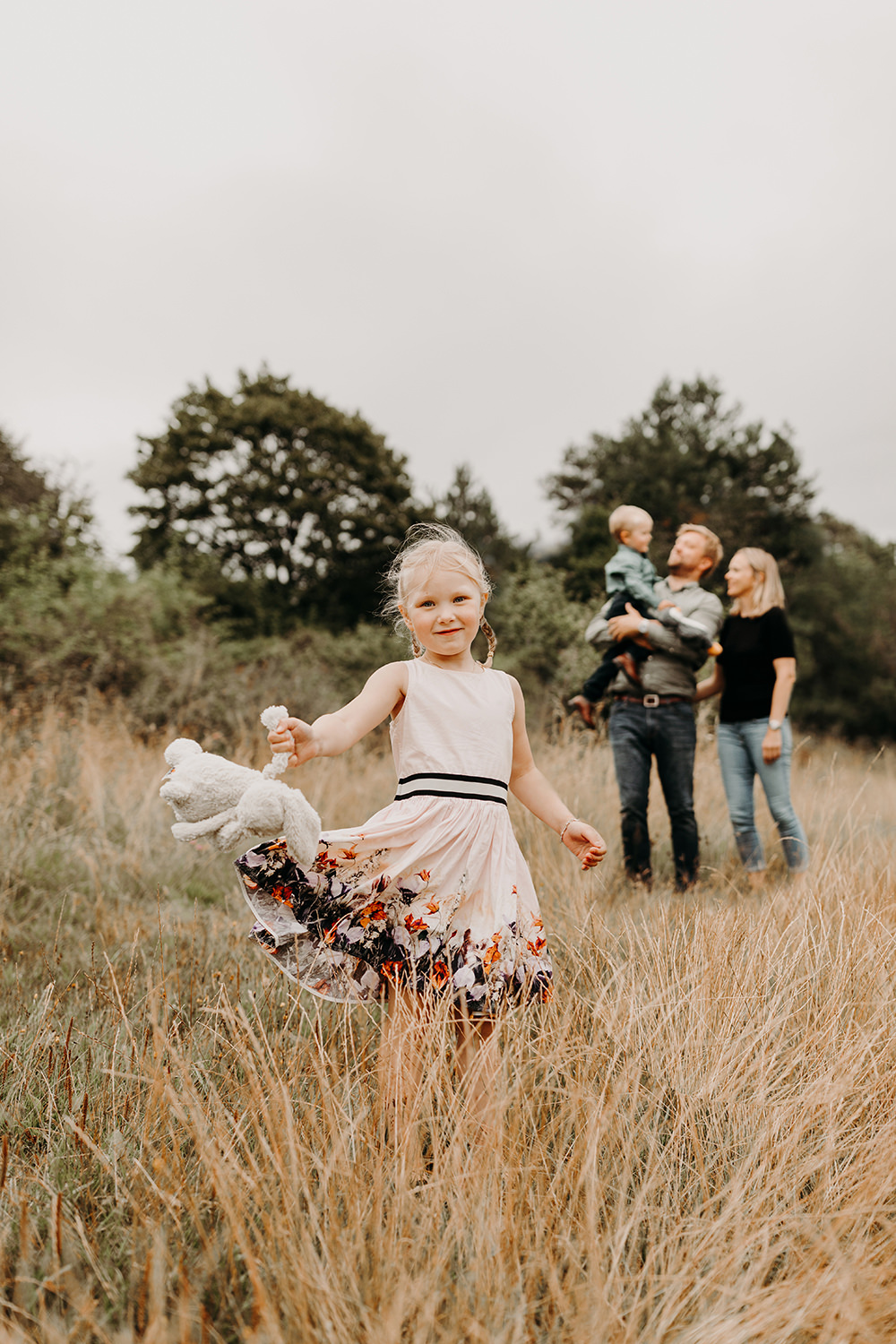 Een gezin in een veld met een klein meisje dat in het gras rent tijdens een gezinsfotoshoot buiten.
