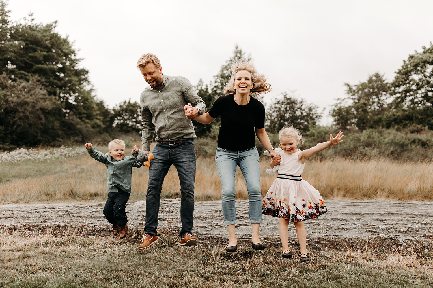 Een gezinsfotoshoot buiten legt een gezin vast dat in het gras in een veld springt.