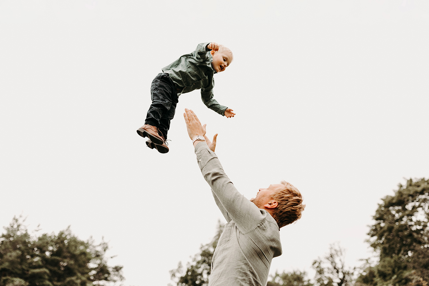 Een man gooit een bal naar zijn zoon in de lucht tijdens een gezinsfotoshoot buiten.