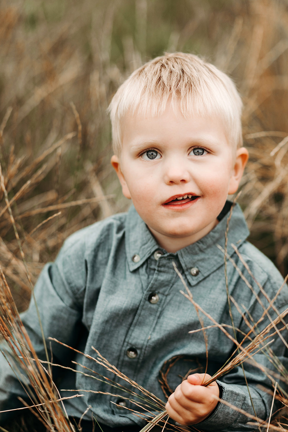 Een jonge jongen zit in een veld tijdens een gezinsfotoshoot buiten.