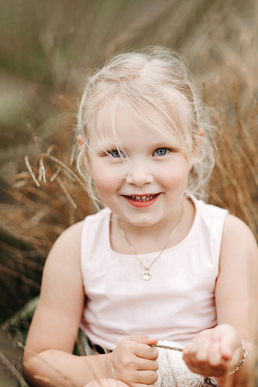 Een klein meisje lacht tijdens een gezinsfotoshoot buiten in hoog gras.