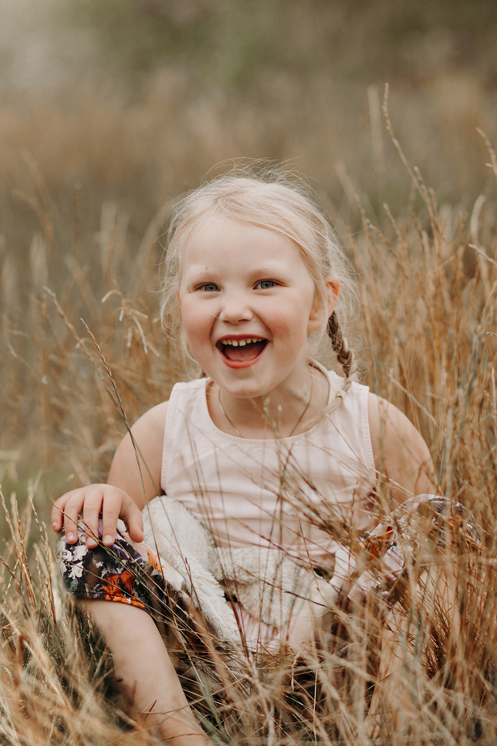 Een klein meisje lacht tijdens een gezinsfotoshoot buiten in hoog gras.