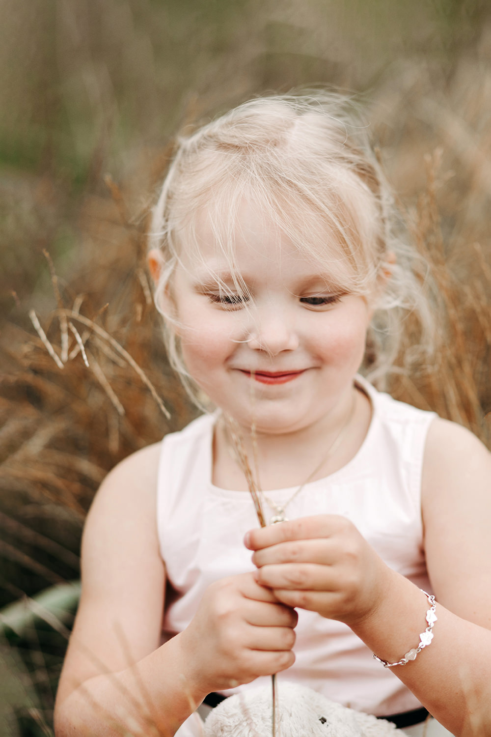 Gezinsfotoshoot buiten met een klein meisje dat een bloem vasthoudt in een grasveld.