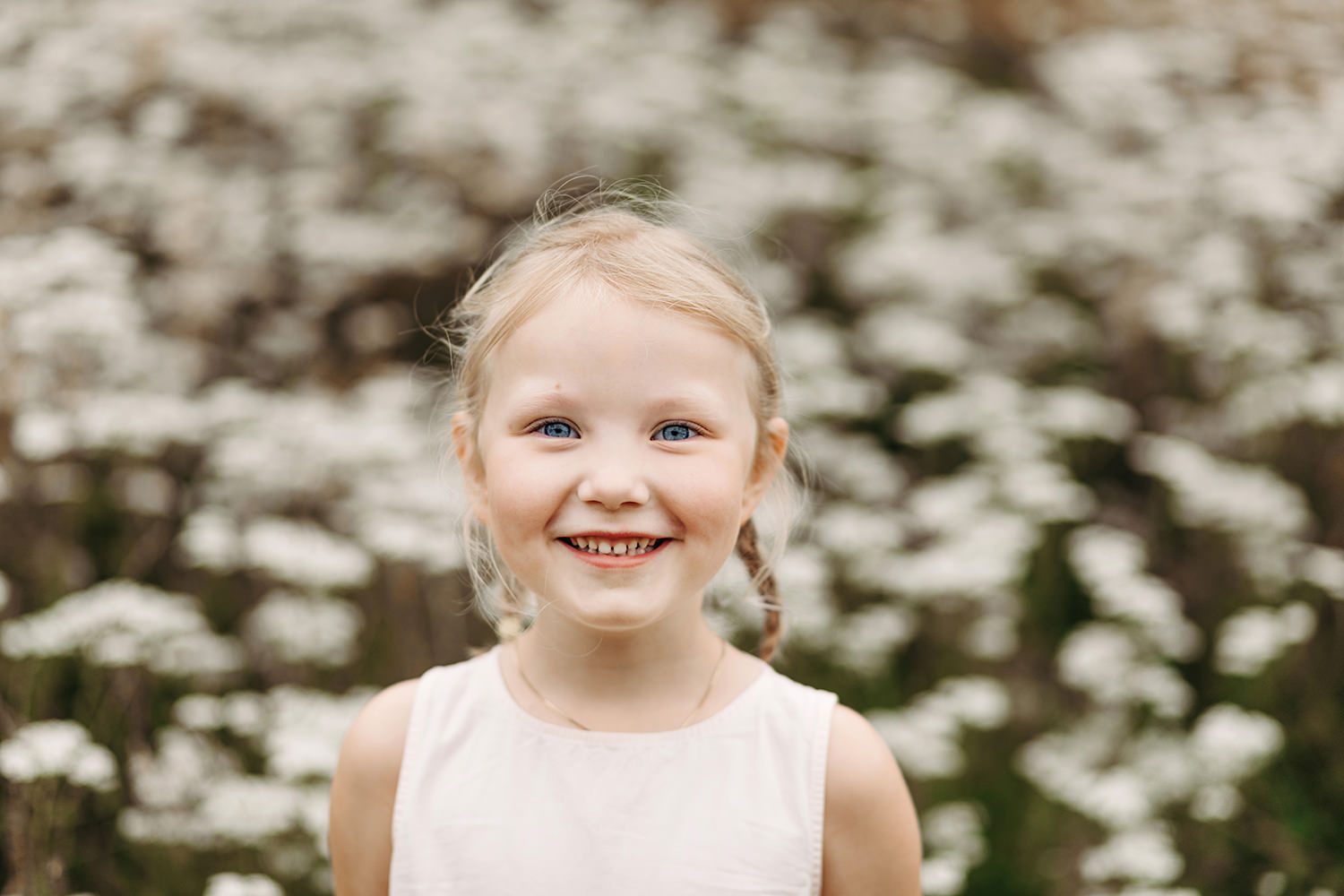 Een klein meisje glimlachend in een veld met bloemen tijdens een gezinsfotoshoot buiten.