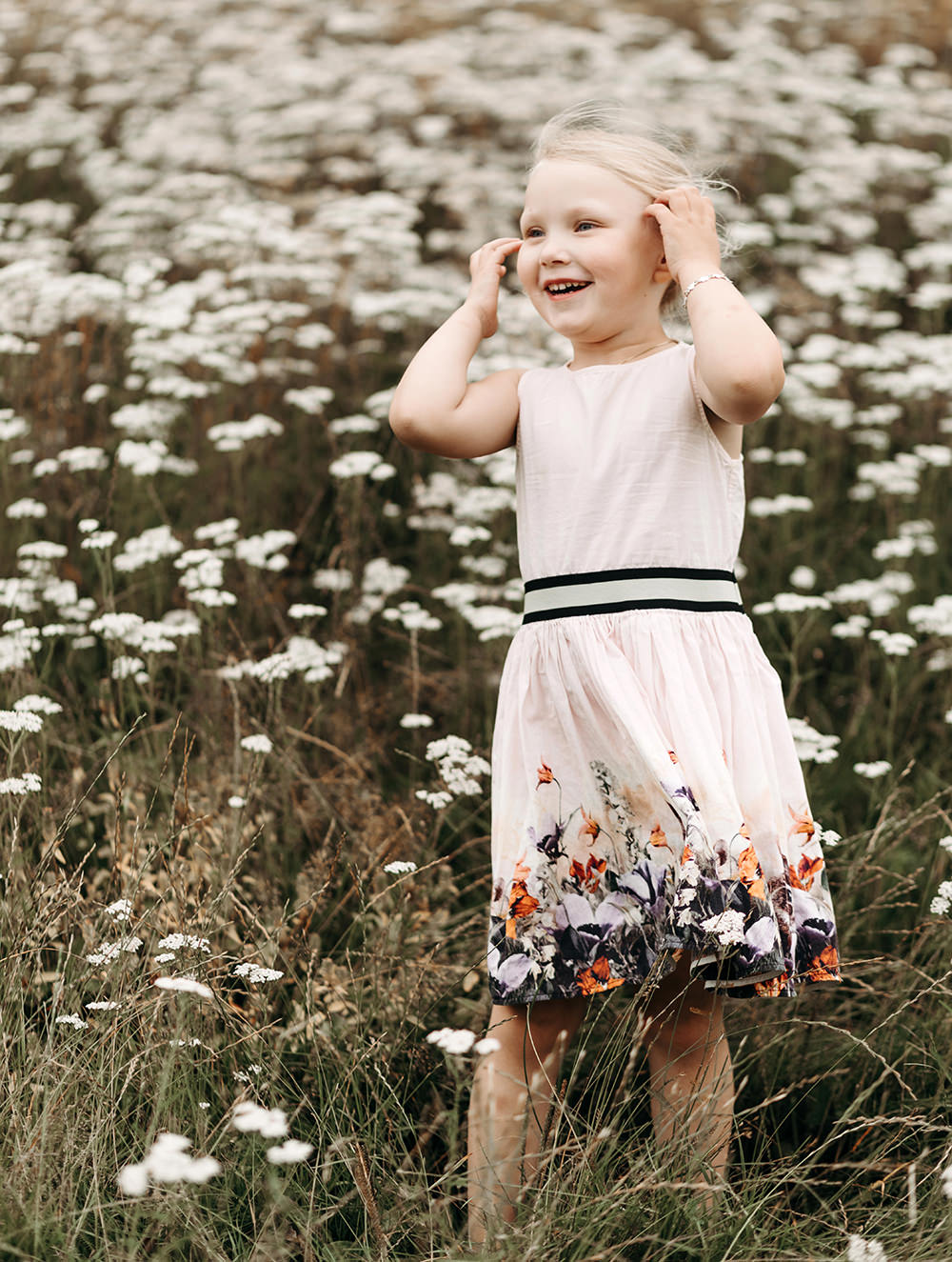 Een klein meisje dat in een veld met madeliefjes staat tijdens een gezinsfotoshoot buiten.