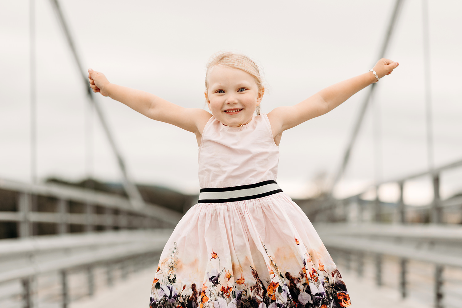 Een klein meisje poseert voor een gezinsfotoshoot buiten op een brug.