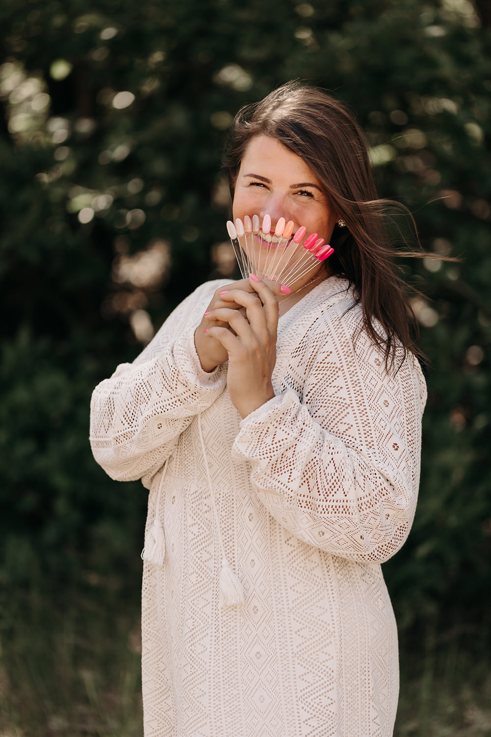 Lifestyle portret van glimlachende nagellak expert in witte jurk en nagellak samples op buitenlocatie tijdens personal branding