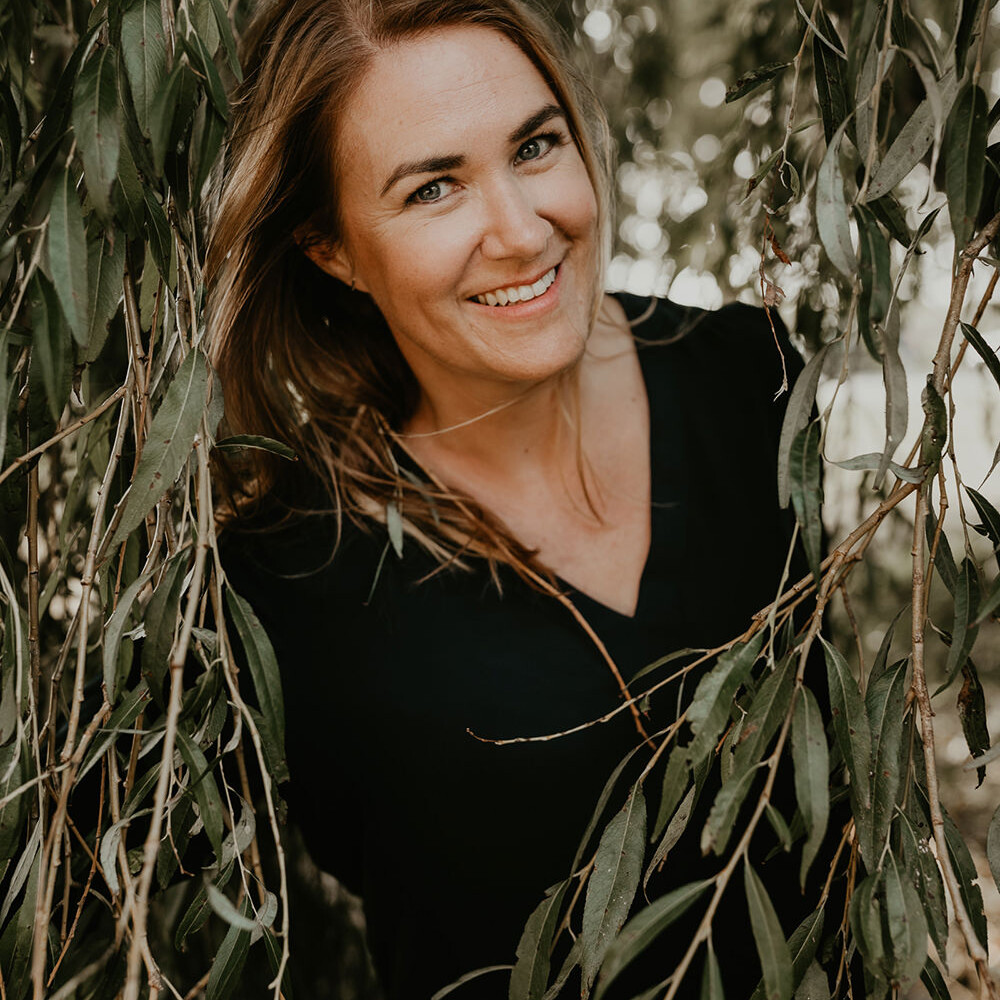 Portret van een glimlachende vrouw tussen de takken tijdens een personal branding fotoshoot