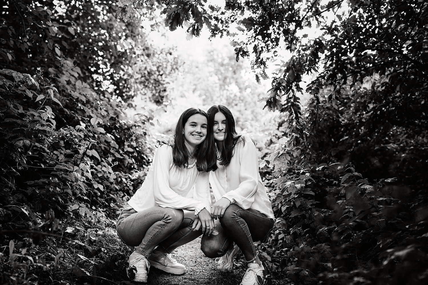 zwart wit foto van twee donkerharige lachende jonge damen poseren in een zussen fotosessie buiten in de Nederlandse natuur