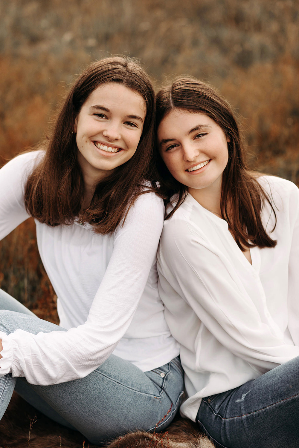 Twee bruinharige lachende jonge zussen poseren in een zussen fotosessie buiten in de Nederlandse natuur
